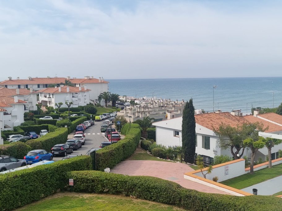 Vista costera con casas blancas, coches aparcados y mar al fondo.