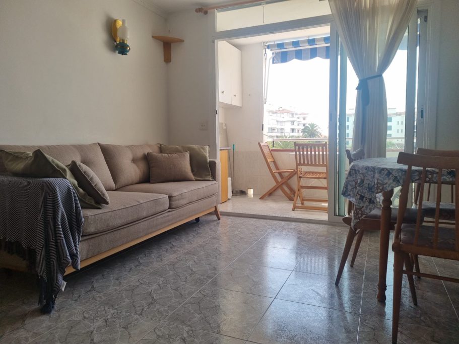 Sala de estar con sofá, mesa de comedor y acceso a un balcón iluminado.