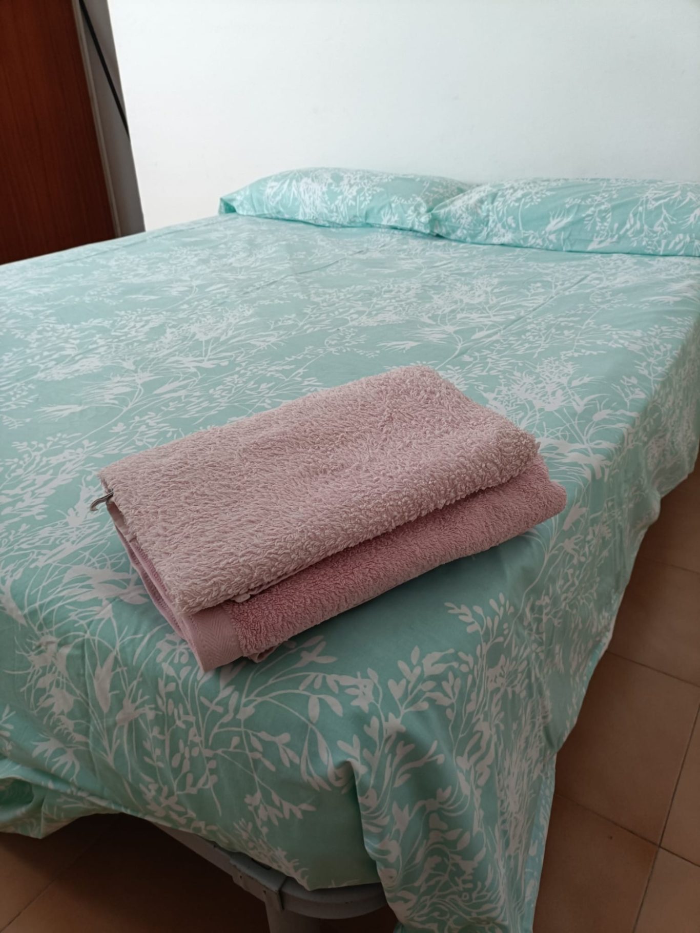 Cama con sábanas turquesas y toallas rosas apiladas al pie.