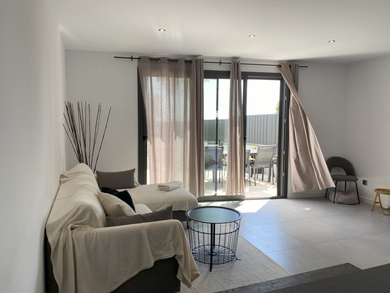 Sala de estar luminosa con sofá, mesa de centro y ventanas con cortinas.