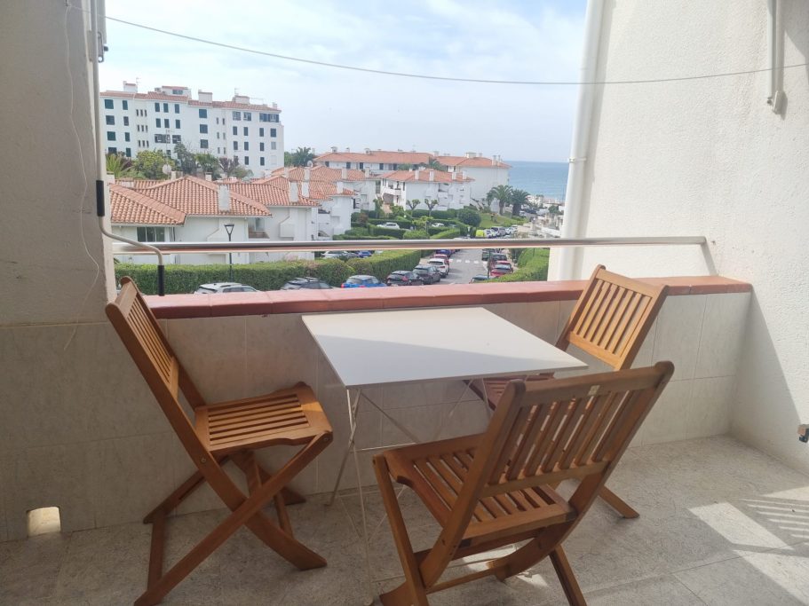 Terraza con mesa y sillas, vista al mar y edificios residenciales cercanos.